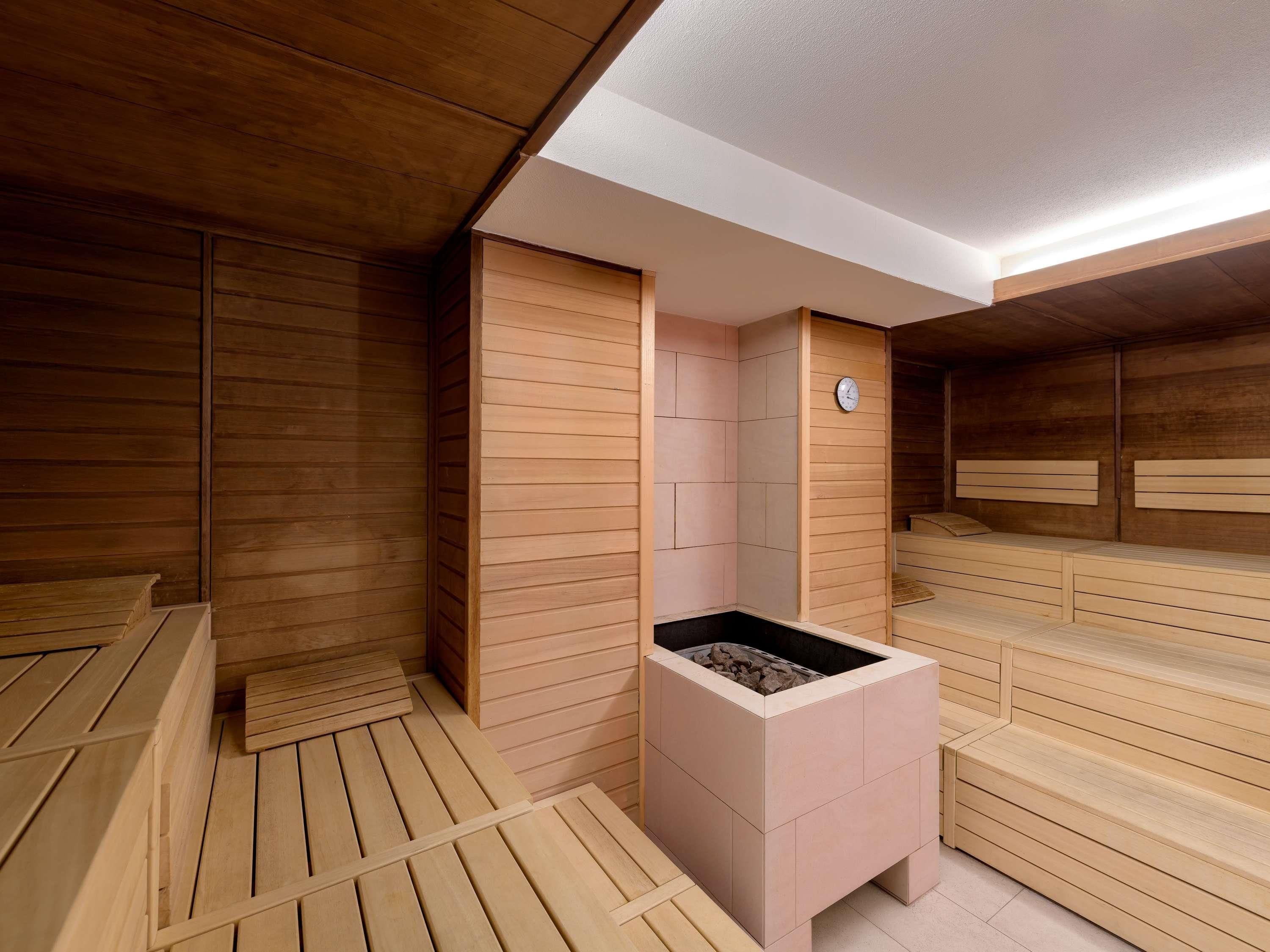 Una sala de sauna con bancos de madera, un calentador central y un reloj en la pared.