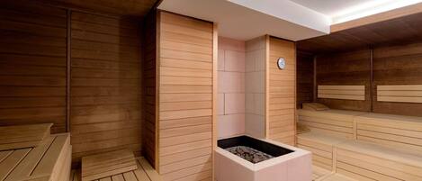 Una sala de sauna con bancos de madera, un calentador central y un reloj en la pared.