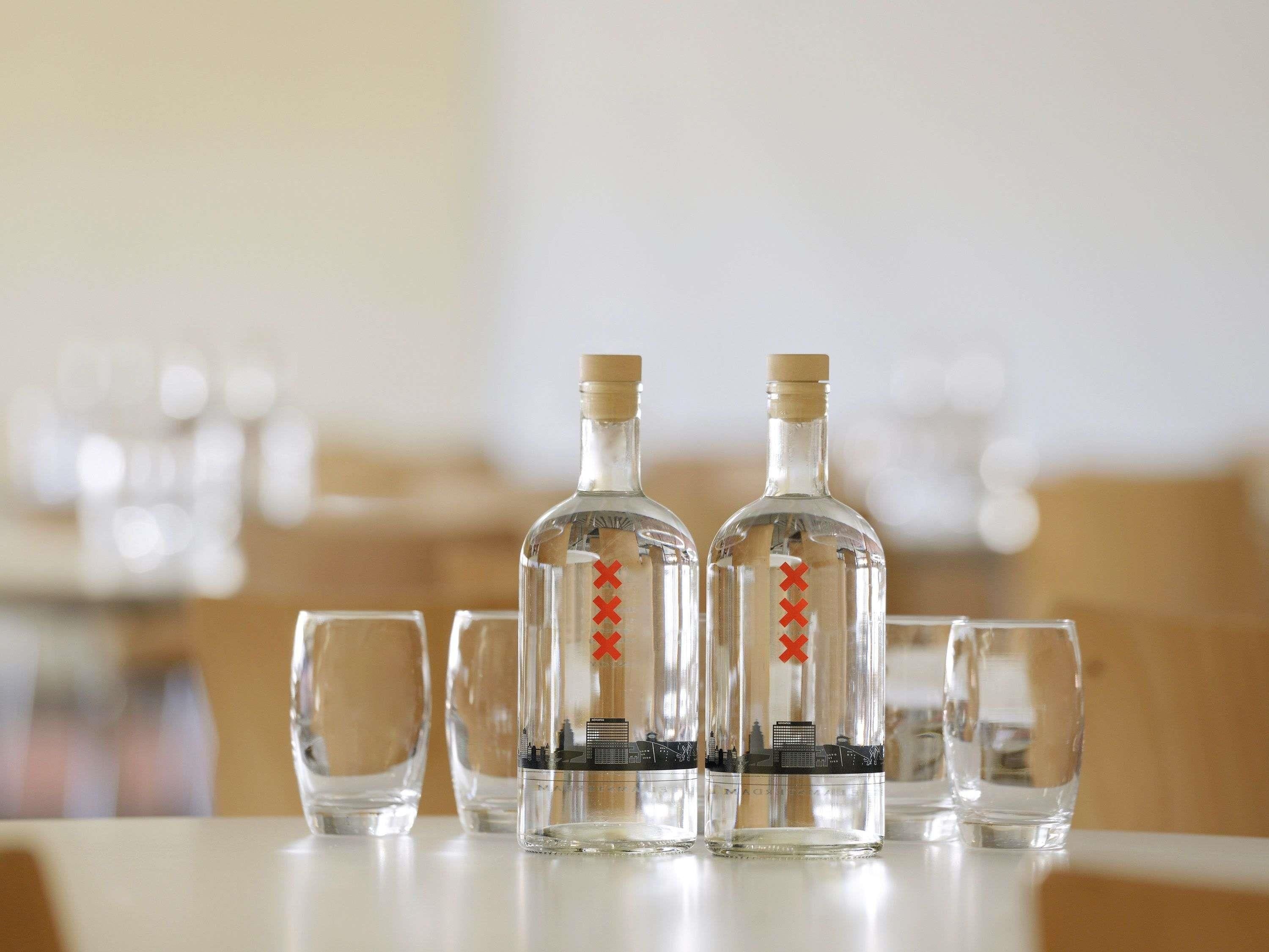 Trois bouteilles en verre transparent, ornées de marques rouges, sont posées sur une table, accompagnées de quatre verres vides.
