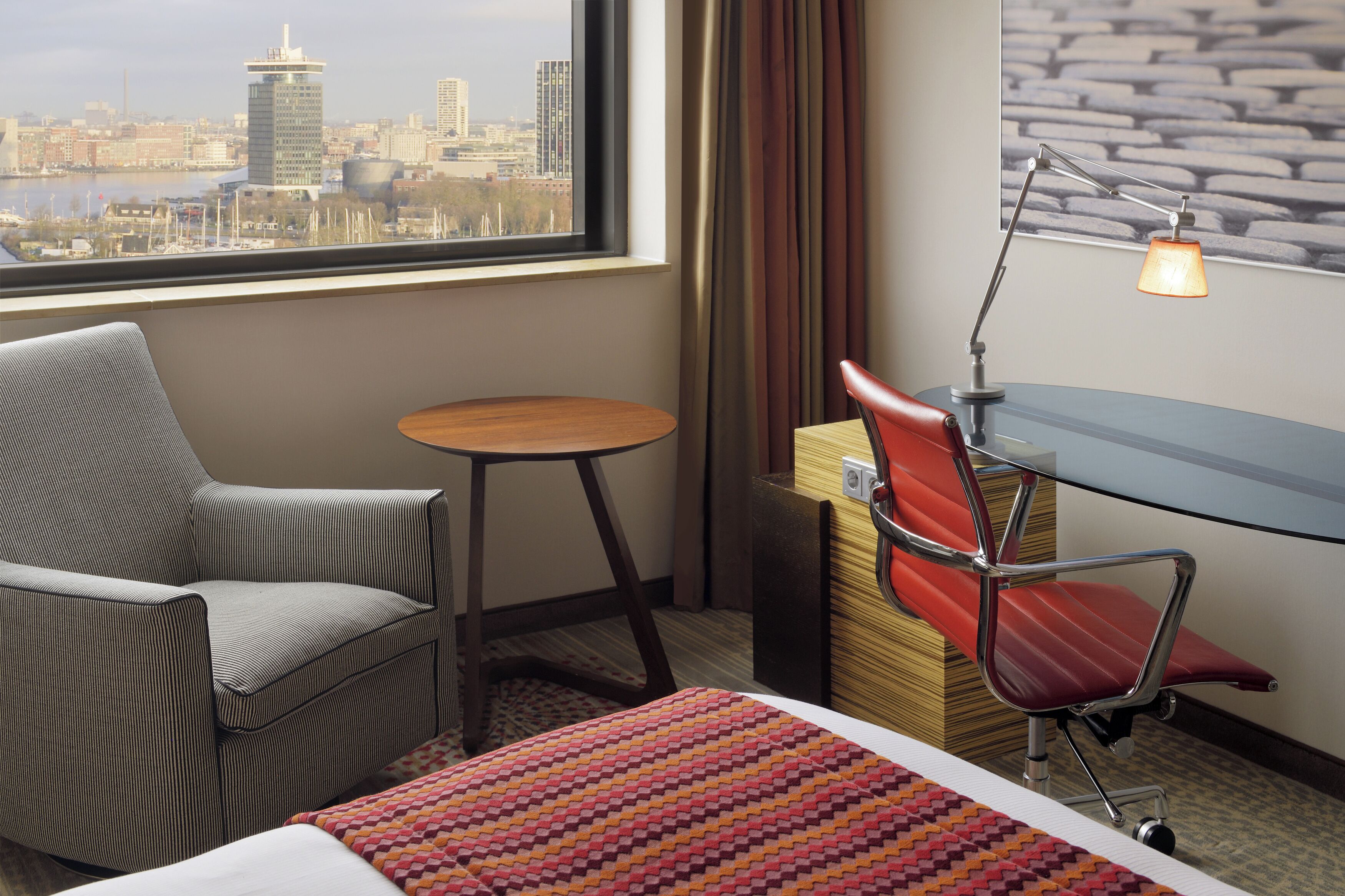 Een hotelkamer met uitzicht over de stad, een bureau, een stoel, een bed en een klein tafeltje.