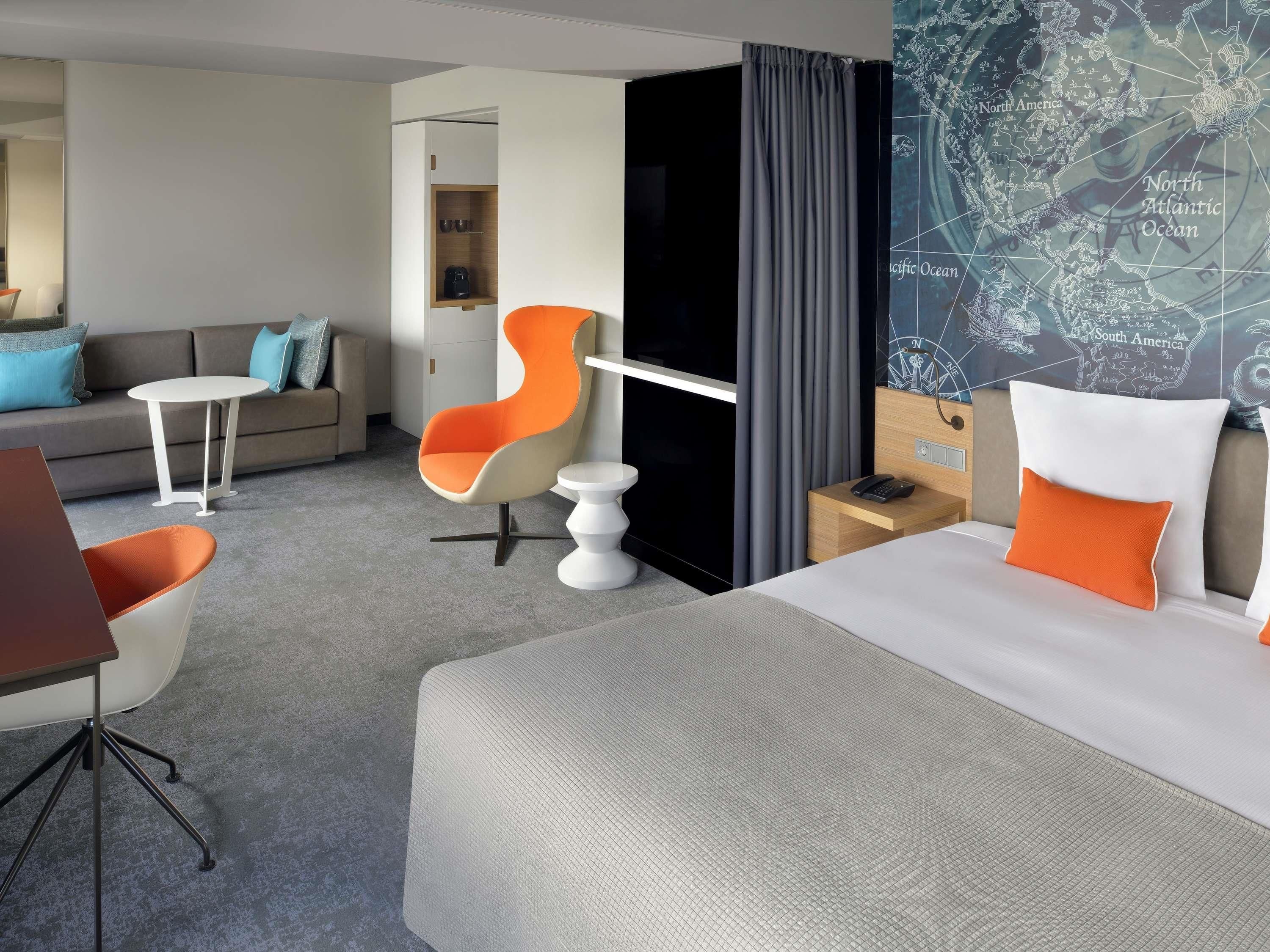Une chambre d’hôtel moderne, équipée d’un lit, d’un bureau, d’une chaise, d’une petite table et d’une carte accrochée au mur.