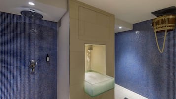 Ein Badezimmer mit blauen Mosaikfliesen, einer Duschkabine aus Glas, einer beige gestrichenen Wand und einer Deckenleuchte.