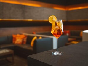 A cocktail glass with a lemon slice on a bar counter in a dimly lit room with a modern design. - Mövenpick Hotel Amsterdam City Centre (Amsterdam)