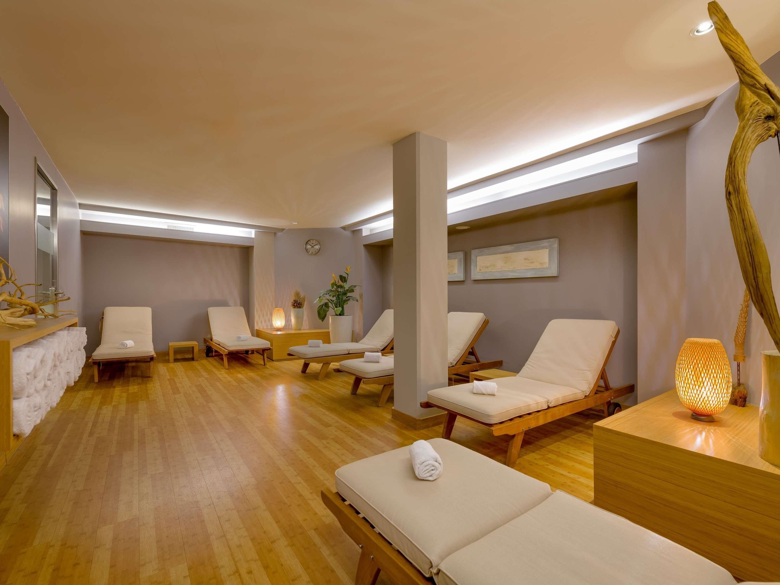 A spa room with wooden floors, multiple lounge chairs, a reception desk, and a wall clock.