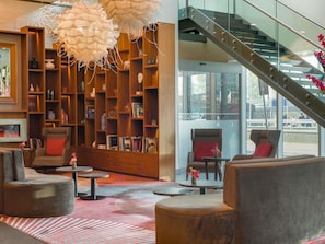 Un interior moderno con una amplia estantería de madera, asientos cómodos y una escalera que conduce a un nivel superior.