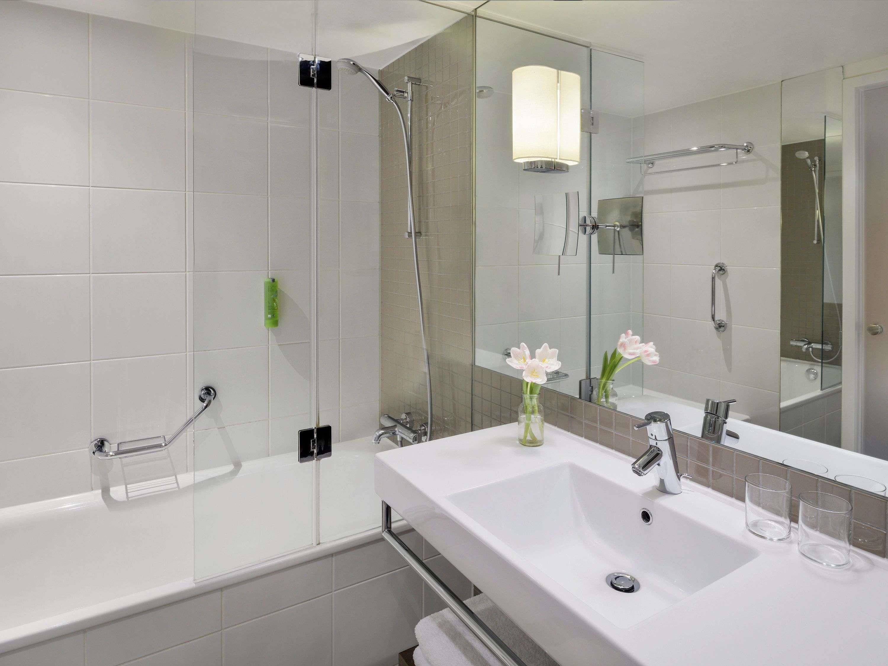 Un baño moderno con ducha de vidrio, un lavabo blanco y un espejo que refleja la zona de la ducha.