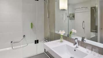 Un baño moderno con ducha de vidrio, un lavabo blanco y un espejo que refleja la zona de la ducha.