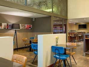 A modern restaurant with wooden paneling, blue chairs, and a bar area with stools. - Mövenpick Hotel Amsterdam City Centre (Amsterdam)