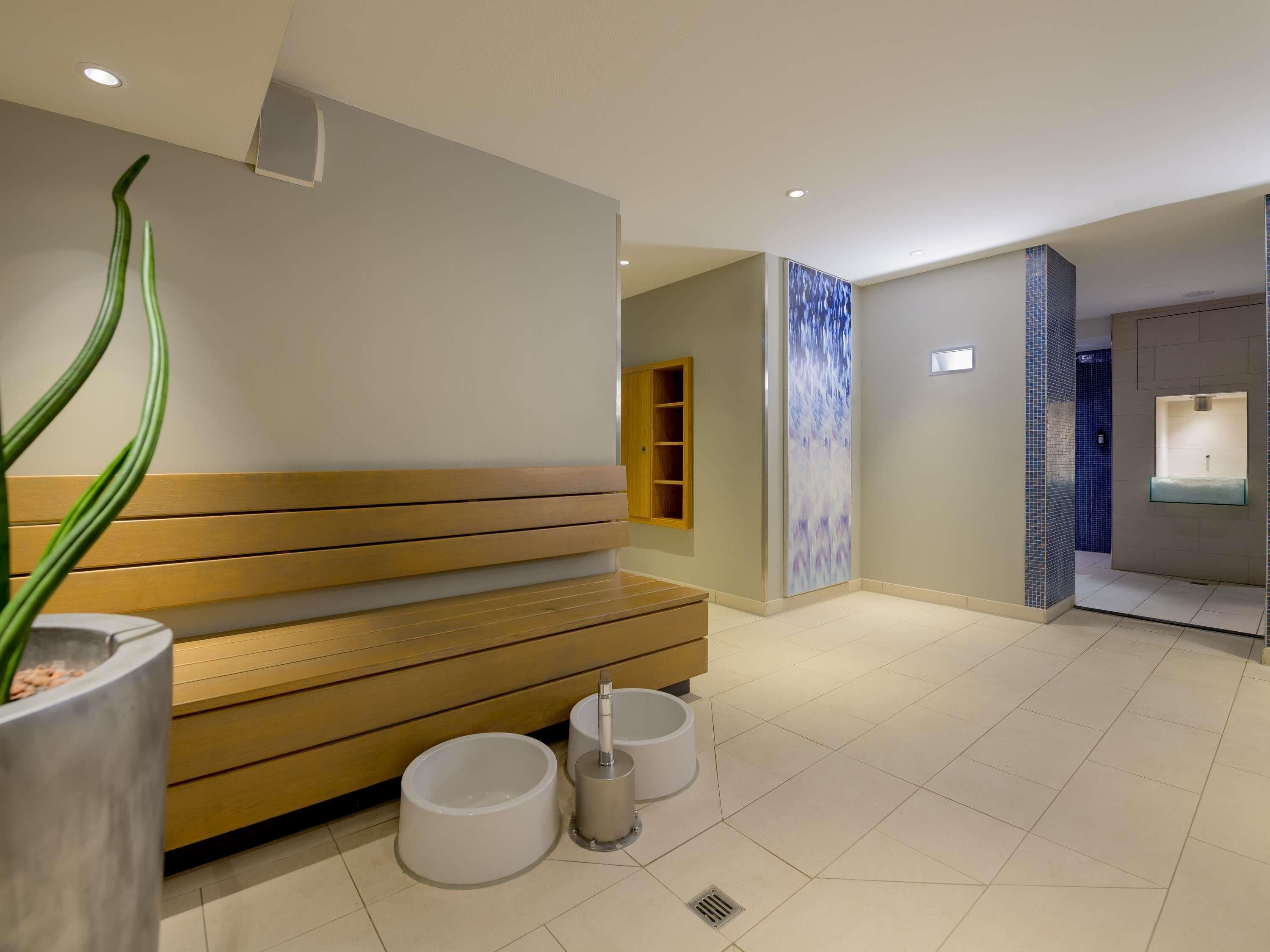 Ein modernes Badezimmer mit einer Holzbank, einem wandmontierten Waschbecken und einem großen abstrakten Wandbild.
