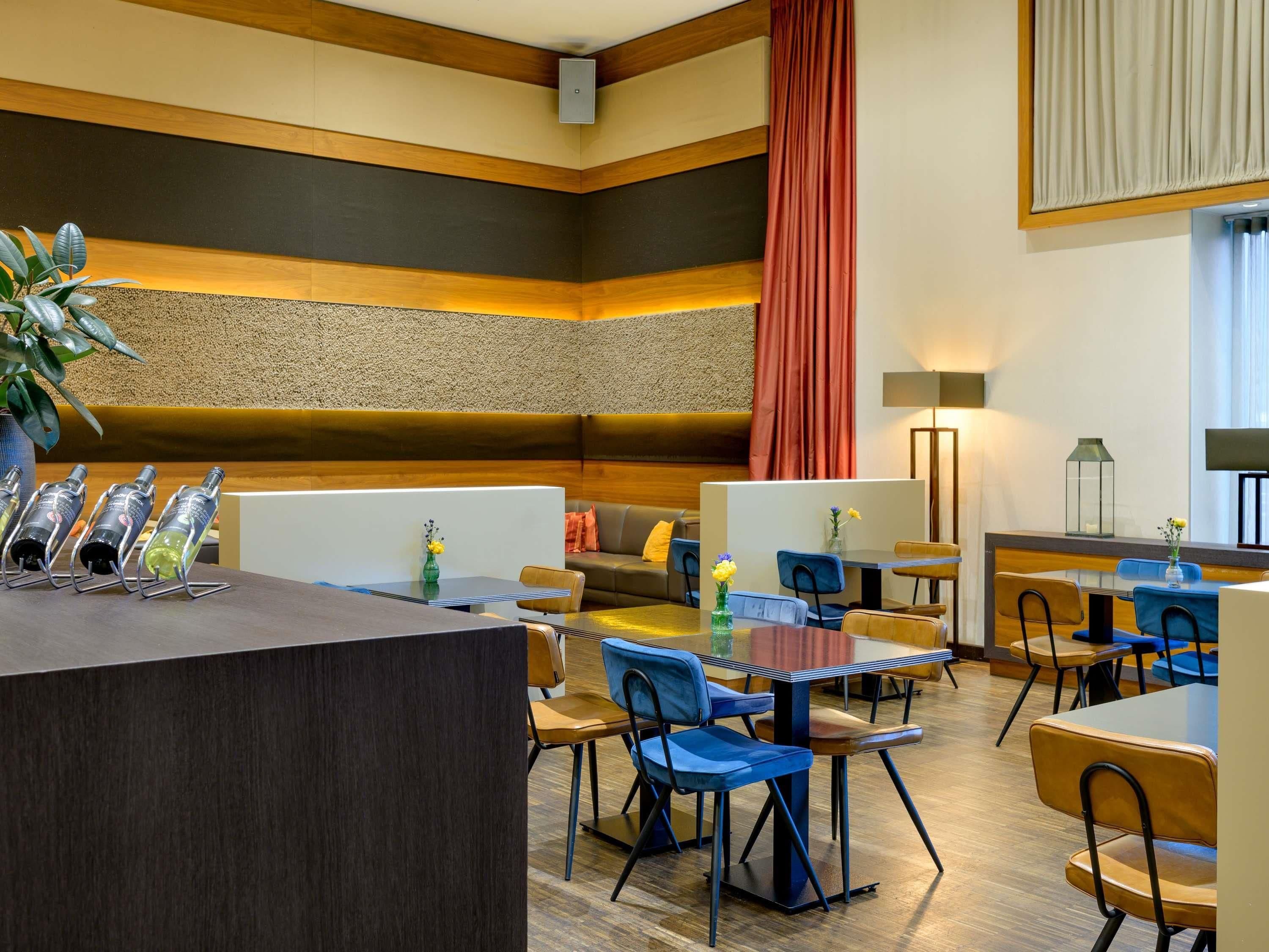 Un hall d’hôtel moderne avec un comptoir d’accueil, des espaces de détente et une grande fenêtre agrémentée de rideaux.