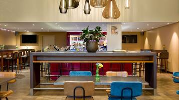 Un moderno vestíbulo de hotel con una zona de bar central, áreas de descanso e iluminación decorativa.