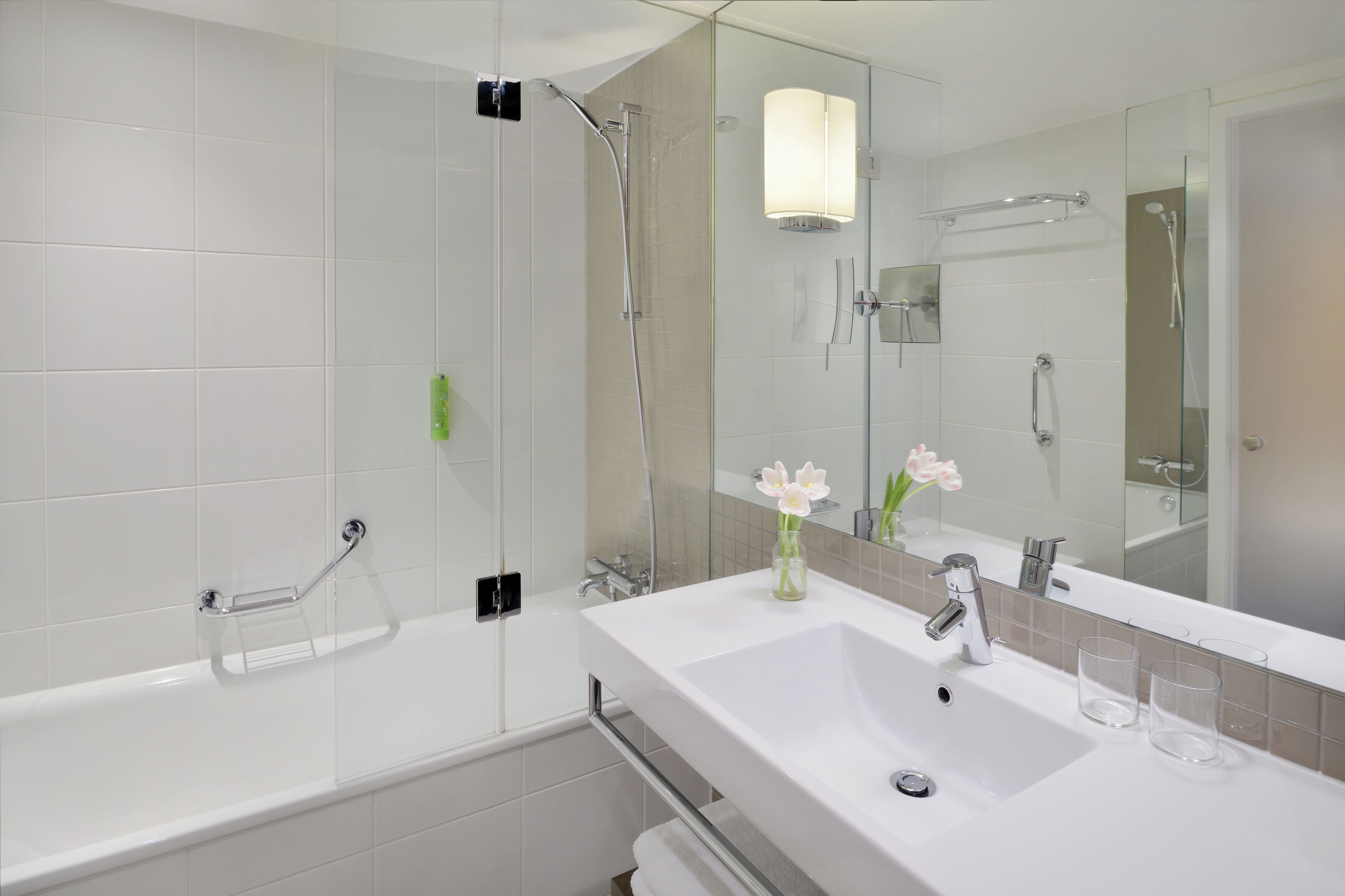 A modern bathroom with a glass shower enclosure, a white sink with a mirror, and a vase with flowers.