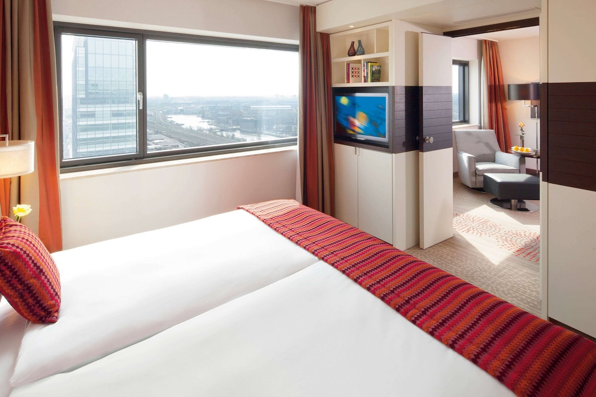 Una habitación de hotel con cama, televisión, escritorio y vistas a la ciudad.