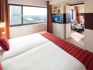 Una habitación de hotel con cama, televisión, escritorio y vistas a la ciudad.