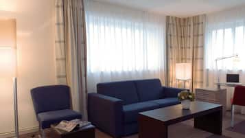 Ein Hotelzimmer mit einem blauen Sofa, einem kleinen Tisch, einem Sessel, einer Lampe und einem Schreibtisch mit einem Laptop.