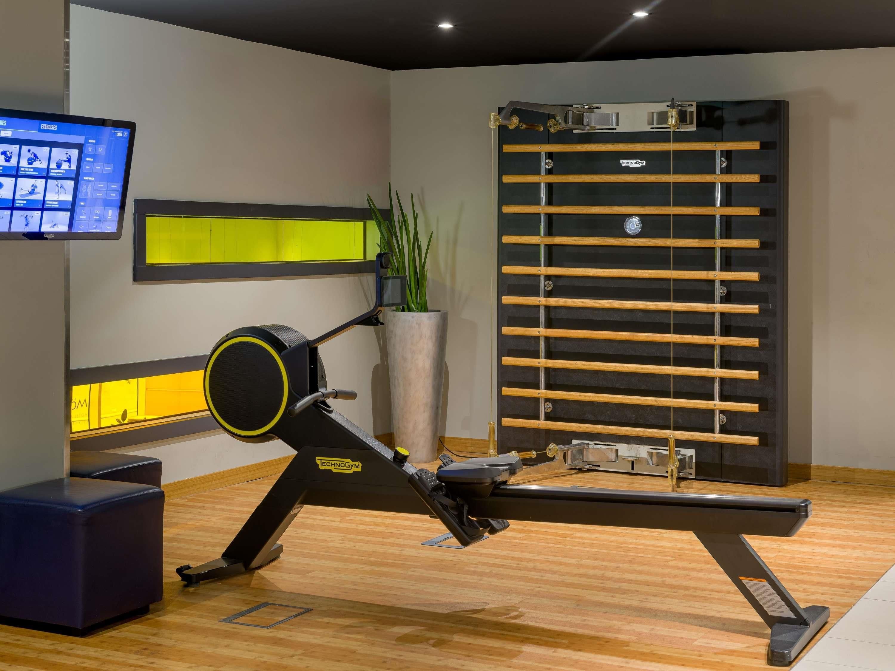 A gym with exercise equipment, a TV screen, and a large planter with green plants.