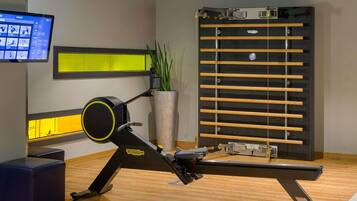 A gym with exercise equipment, a TV screen, and a large planter with green plants.