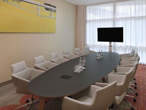 Una sala de conferencias con una gran mesa ovalada, seis sillas, un televisor de pantalla plana y un cuadro en la pared.