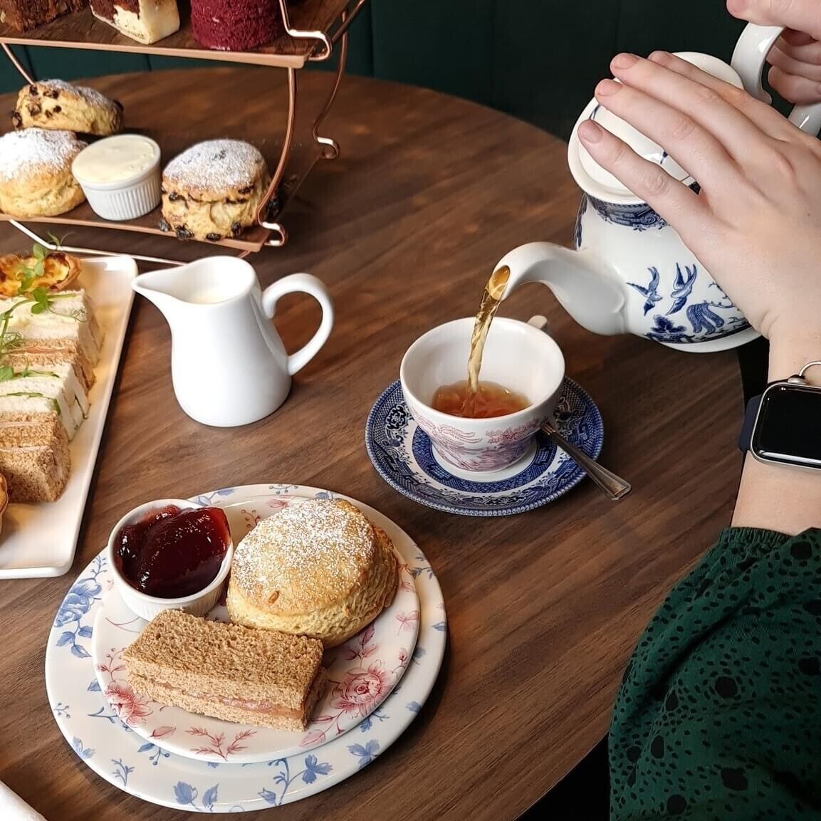 Una mesa dispuesta con té, scones, sándwiches y un plato de postre.