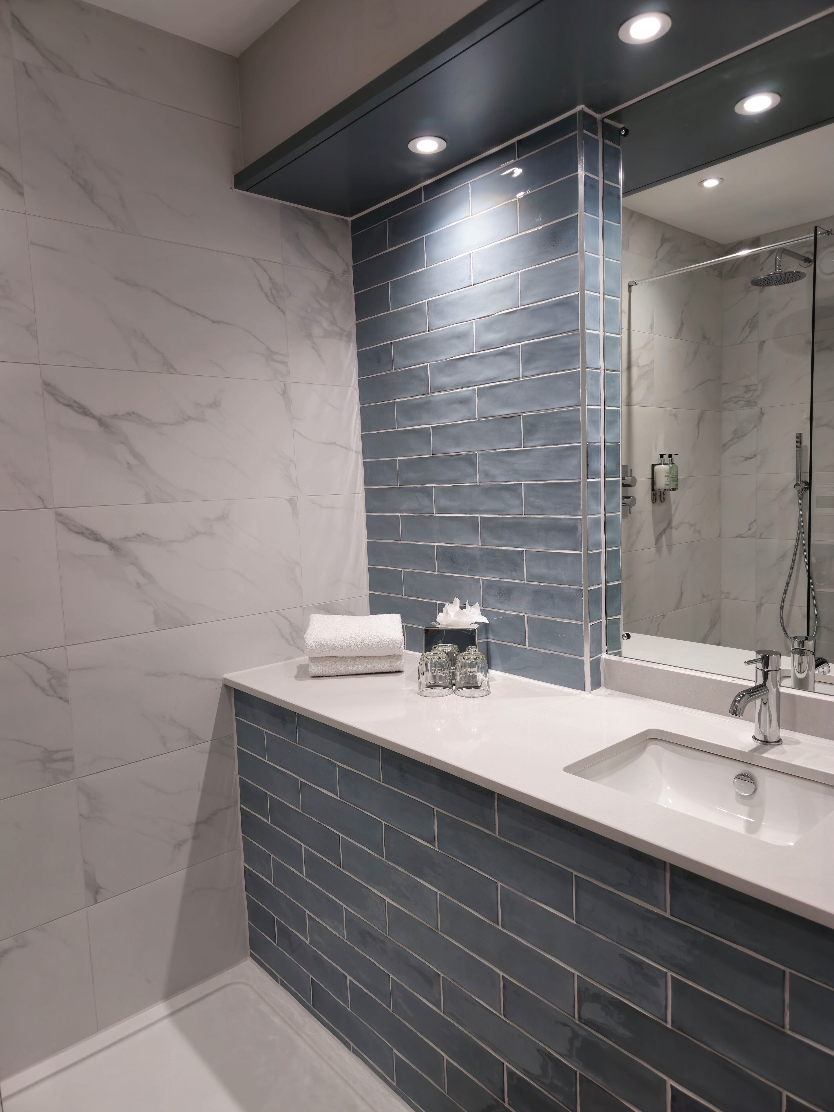Un baño moderno con tocador de mármol blanco, un espejo grande y zona de ducha.