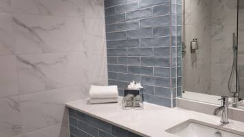 Un baño moderno con tocador de mármol blanco, un espejo grande y zona de ducha.