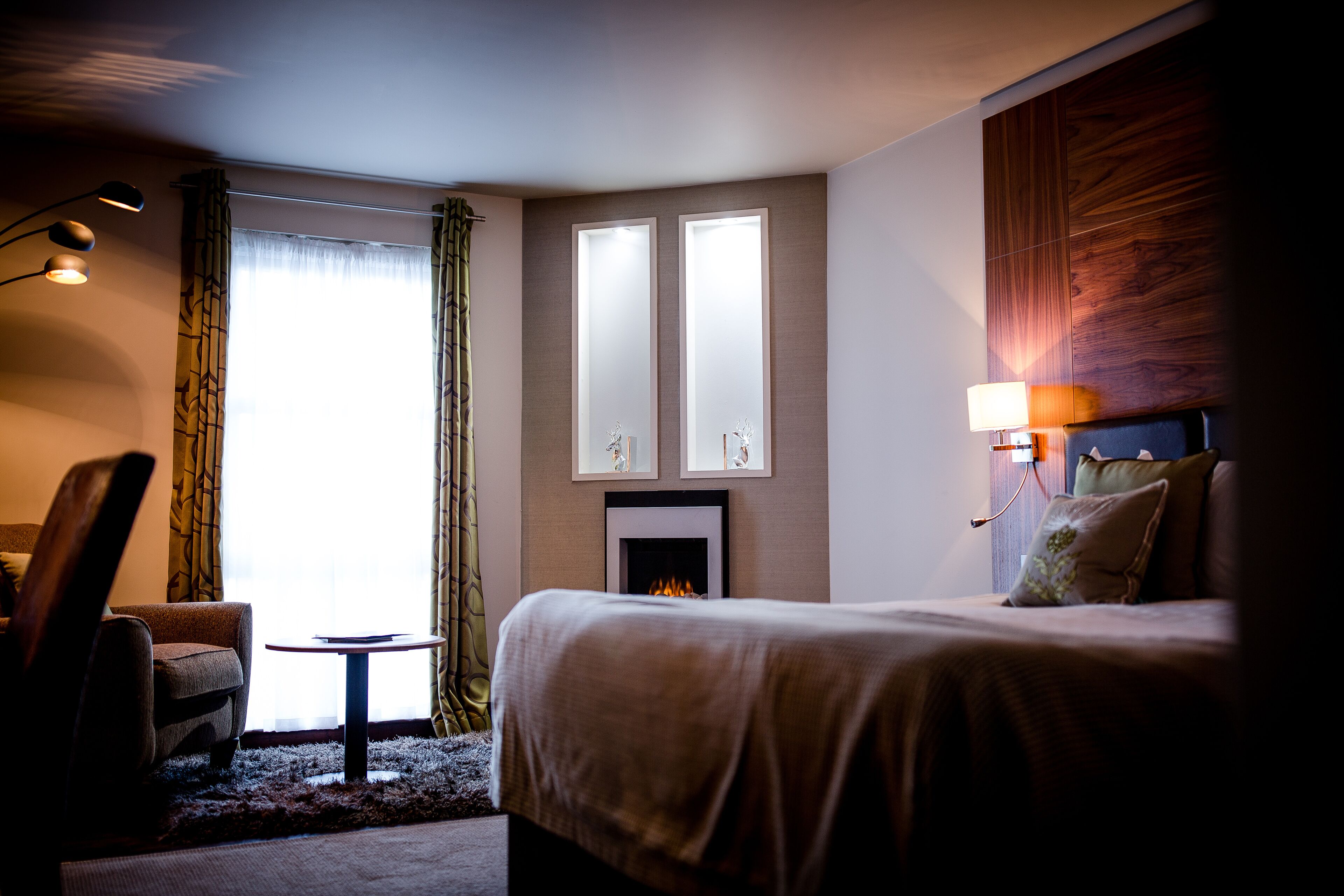 Ein Hotelzimmer mit Bett, Stuhl, kleinem Tisch, Kamin und einem Fenster mit Vorhängen.