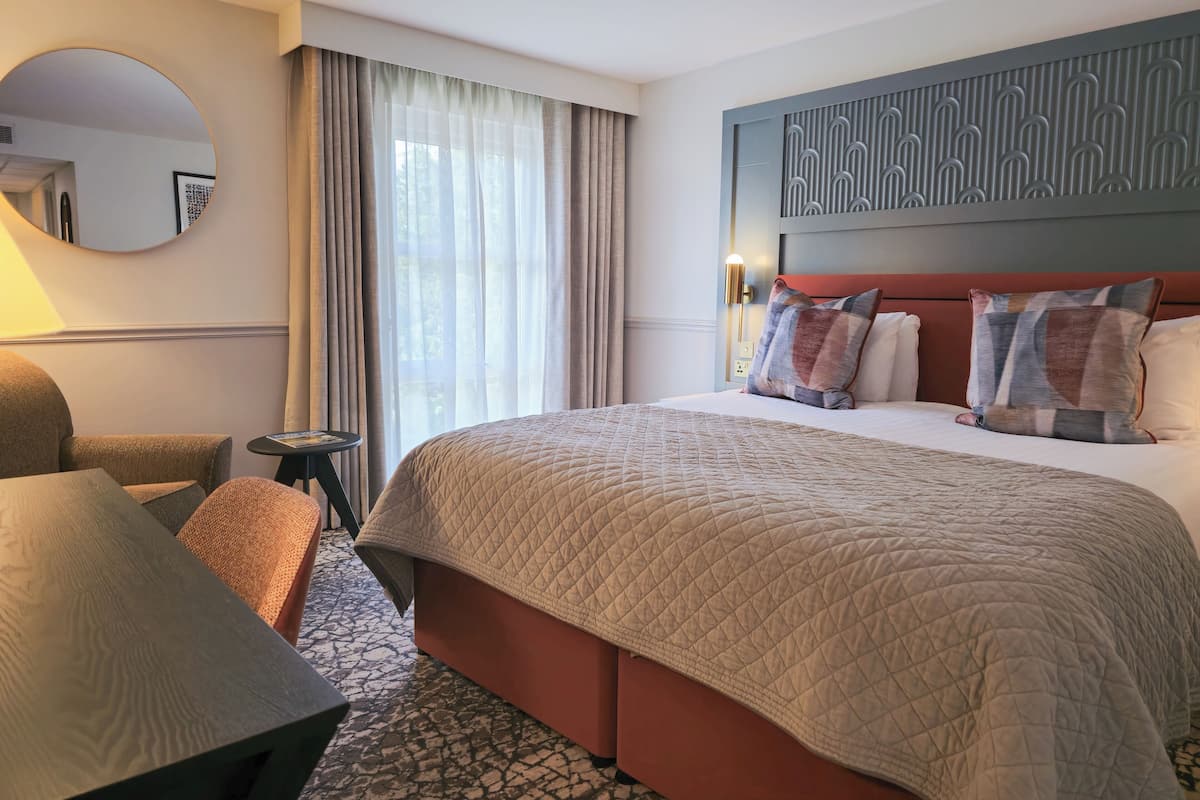A hotel room with a large bed, a round mirror, a small table, and a sofa.