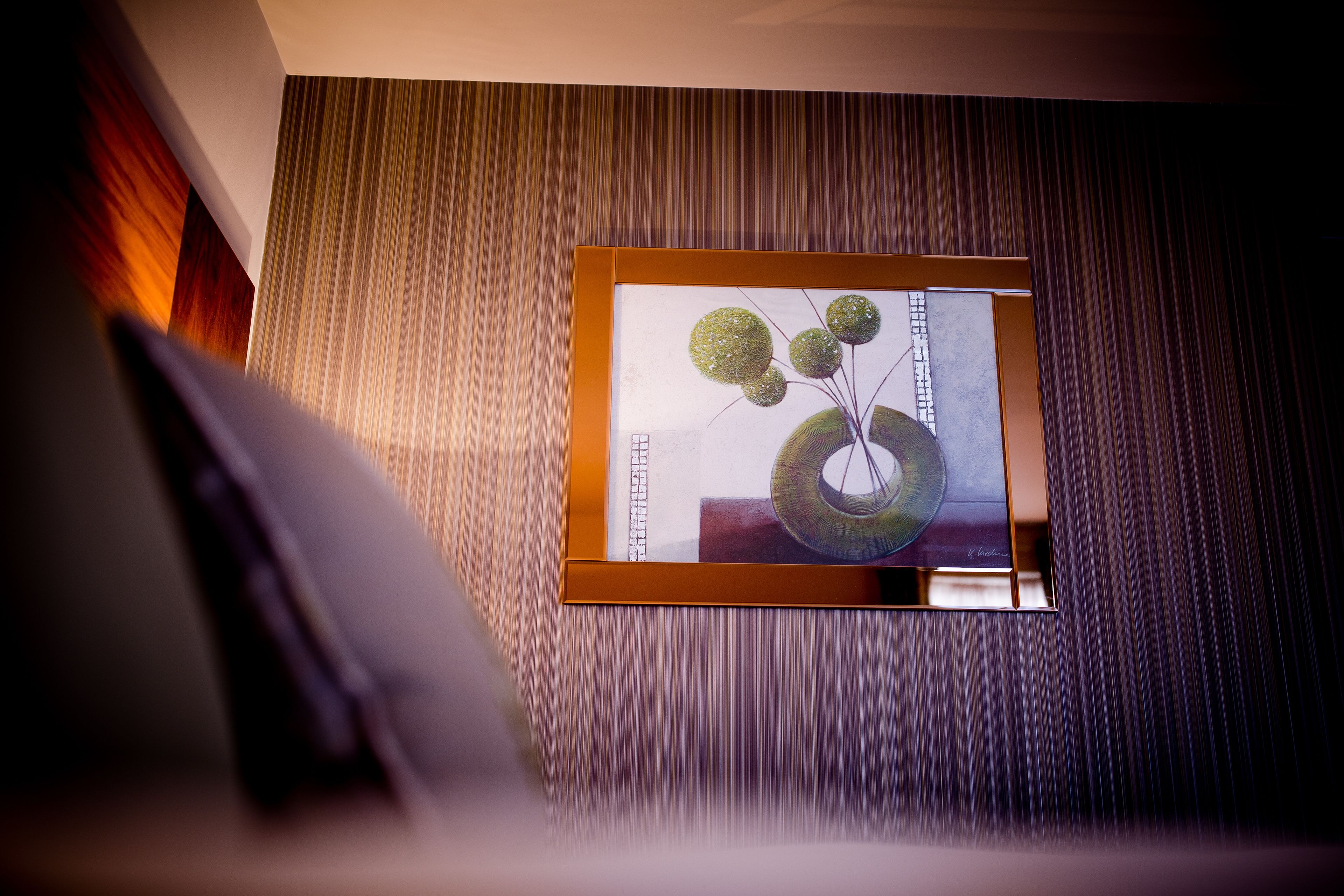 A framed artwork on a wall with vertical lines, a wooden floor, and a partial view of a white object.