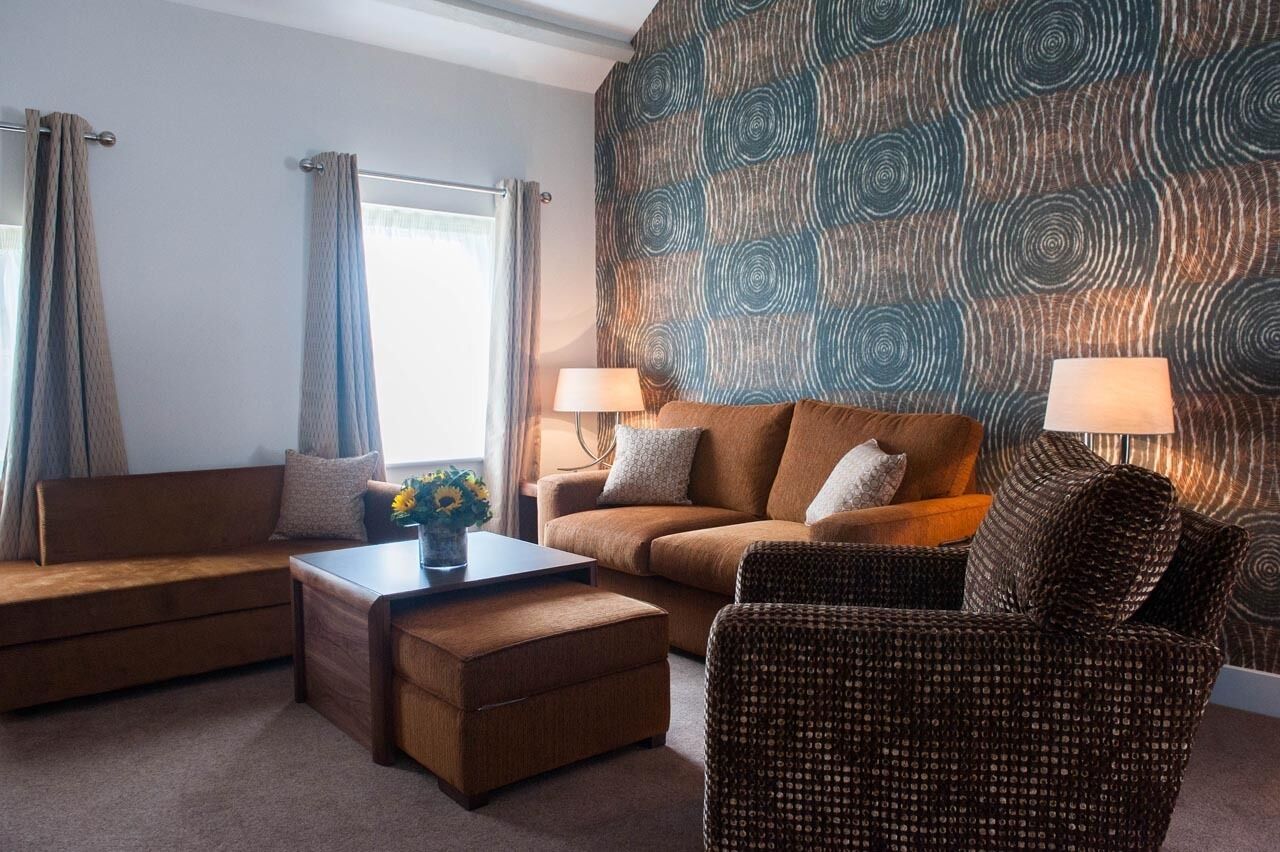 A modern living room with a sofa, ottoman, and armchair, a coffee table, and two lamps.