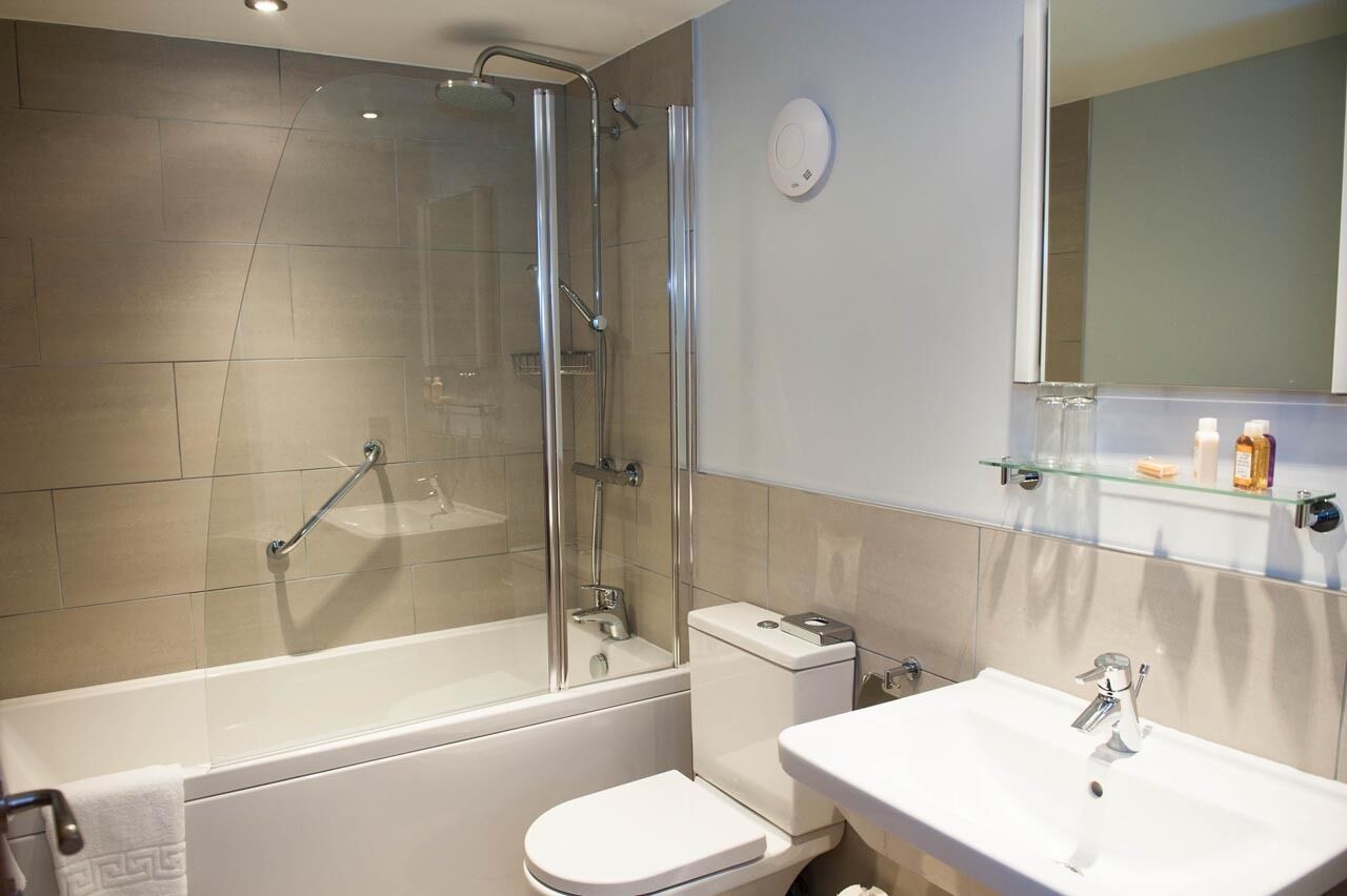 A modern bathroom with a glass-enclosed shower, a white bathtub, a toilet, and a sink with a mirror above.