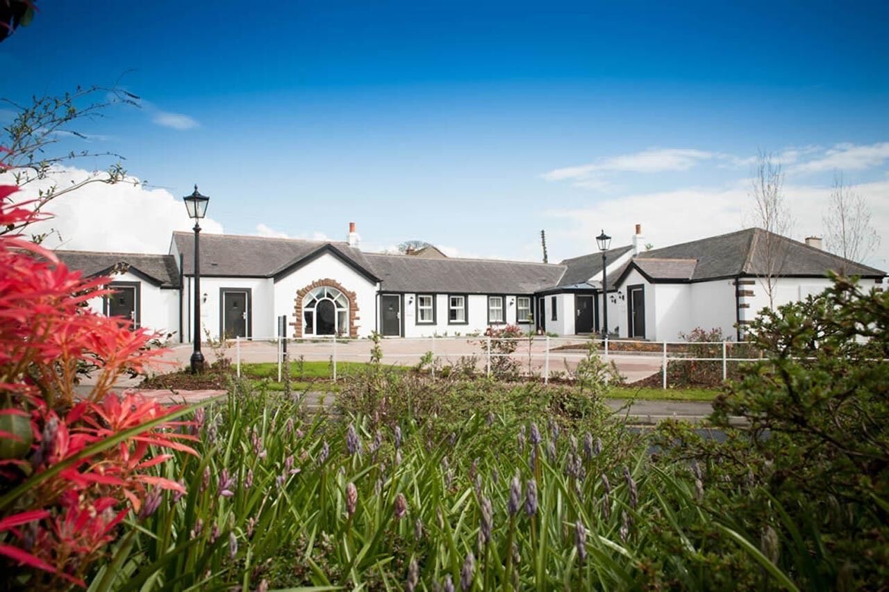 A white building with a central entrance, surrounded by a garden with various plants.