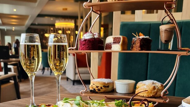 A three-tiered dessert stand with various pastries and a glass of white wine on a table in a restaurant. - Smiths at Gretna Green (Gretna)