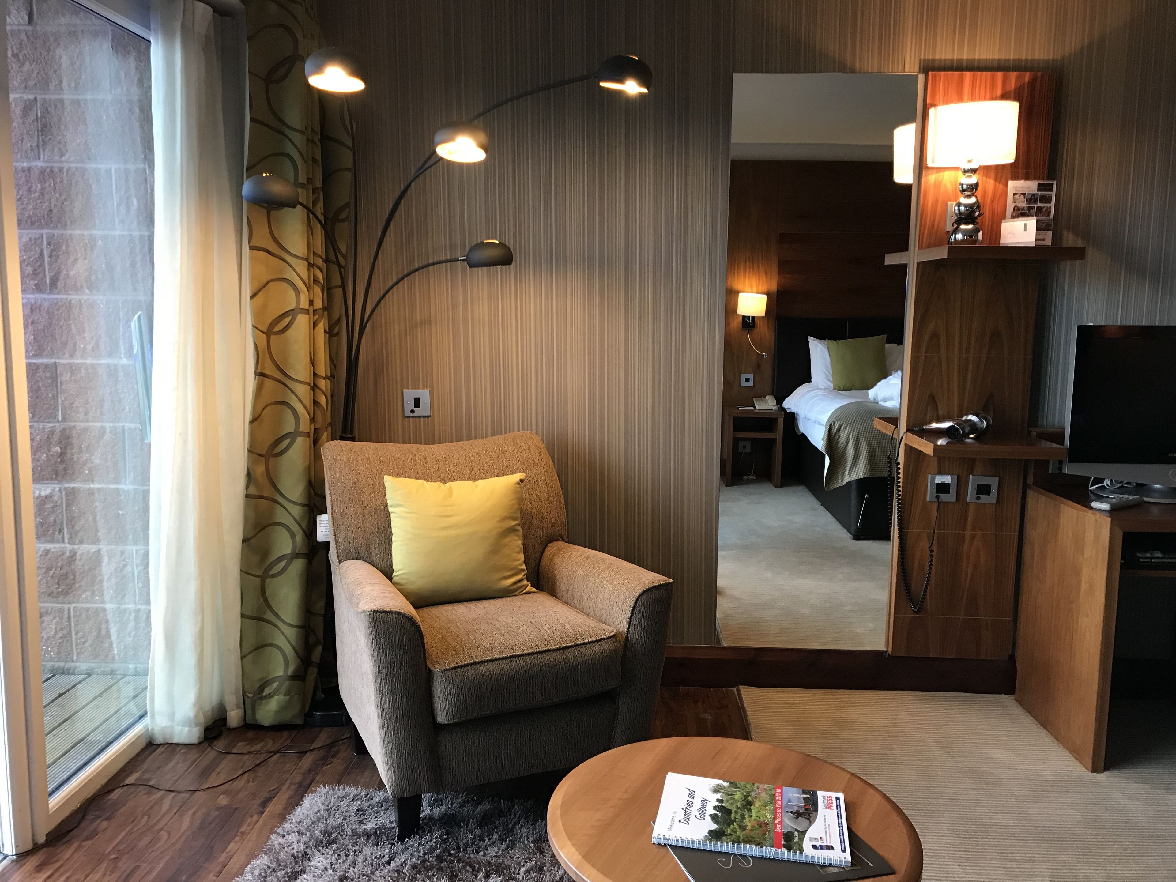 Habitación de hotel con sofá, una mesita con una revista, televisor y un espejo que refleja el cuarto.