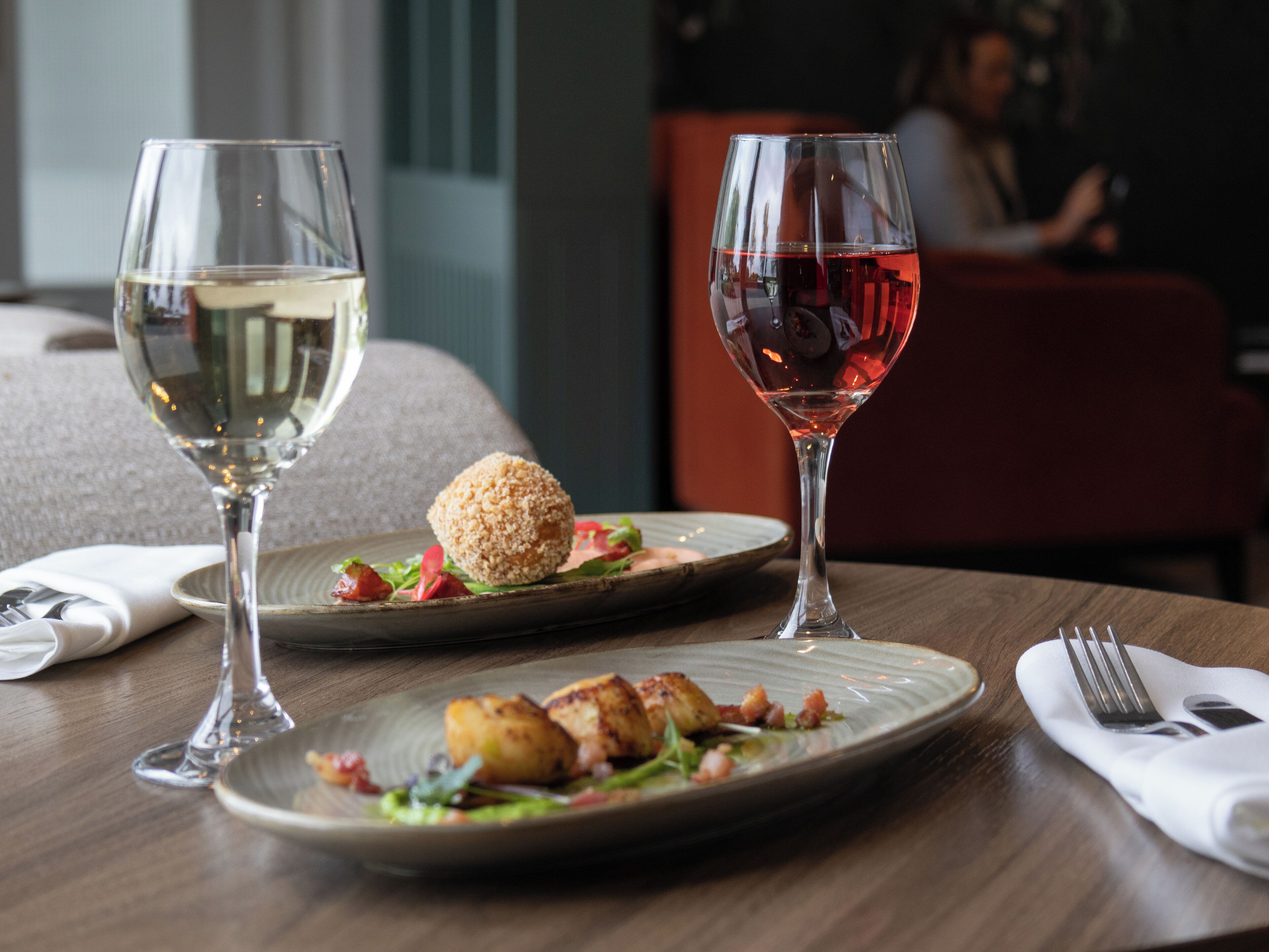 A dining table with two wine glasses, one with white wine and the other with red wine, and a plate of food.