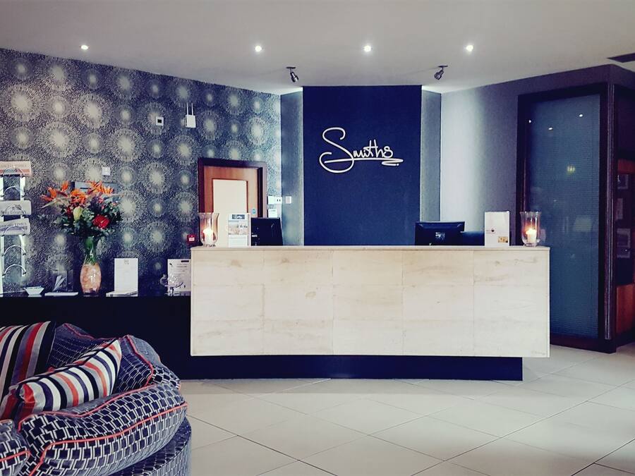 Un'area reception dal design moderno, con una parete blu scuro con su scritto 'Smiths' e un banco reception chiaro. Dietro il banco si nota una parete decorata con un motivo e, in primo piano, un divano con cuscini a righe.