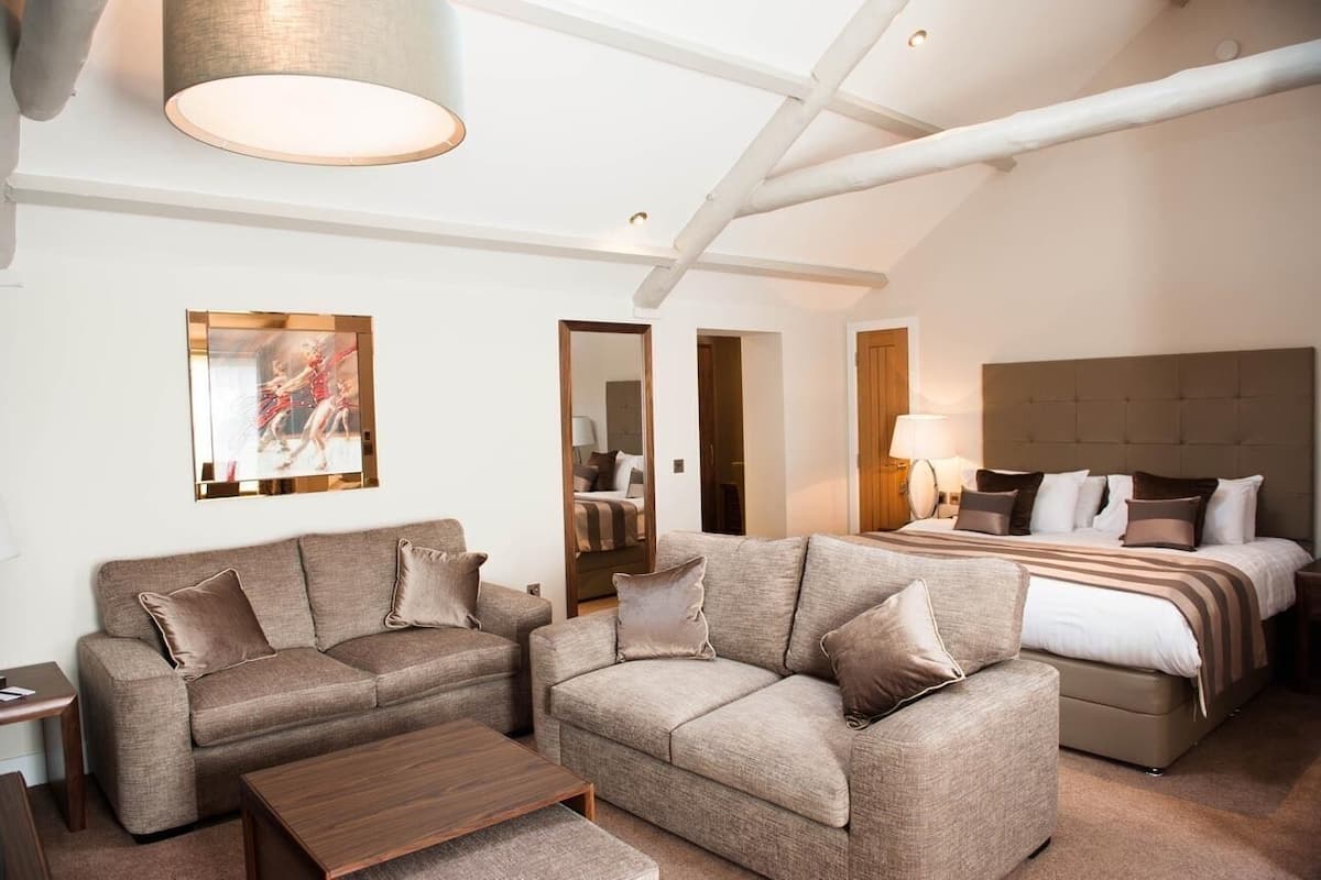 A hotel room with a large bed, two sofas, a coffee table, and a painting on the wall.