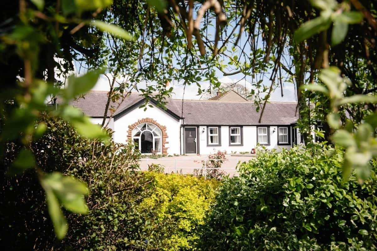 A traditional white building with a black roof, surrounded by lush greenery.