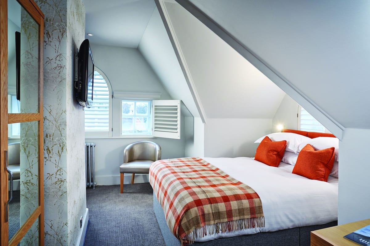 A bedroom with a large bed, a chair, a radiator, and a window with blinds.