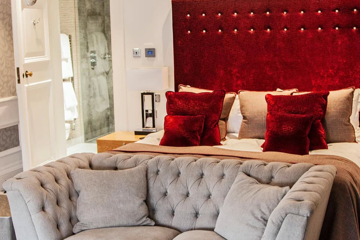 A modern bedroom with a tufted headboard, a grey sofa, and a red accent wall.