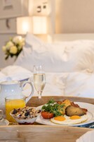 Bandeja de desayuno con huevos, tocino, tostadas y un vaso de zumo de naranja sobre una mesa de madera en una habitación de hotel.