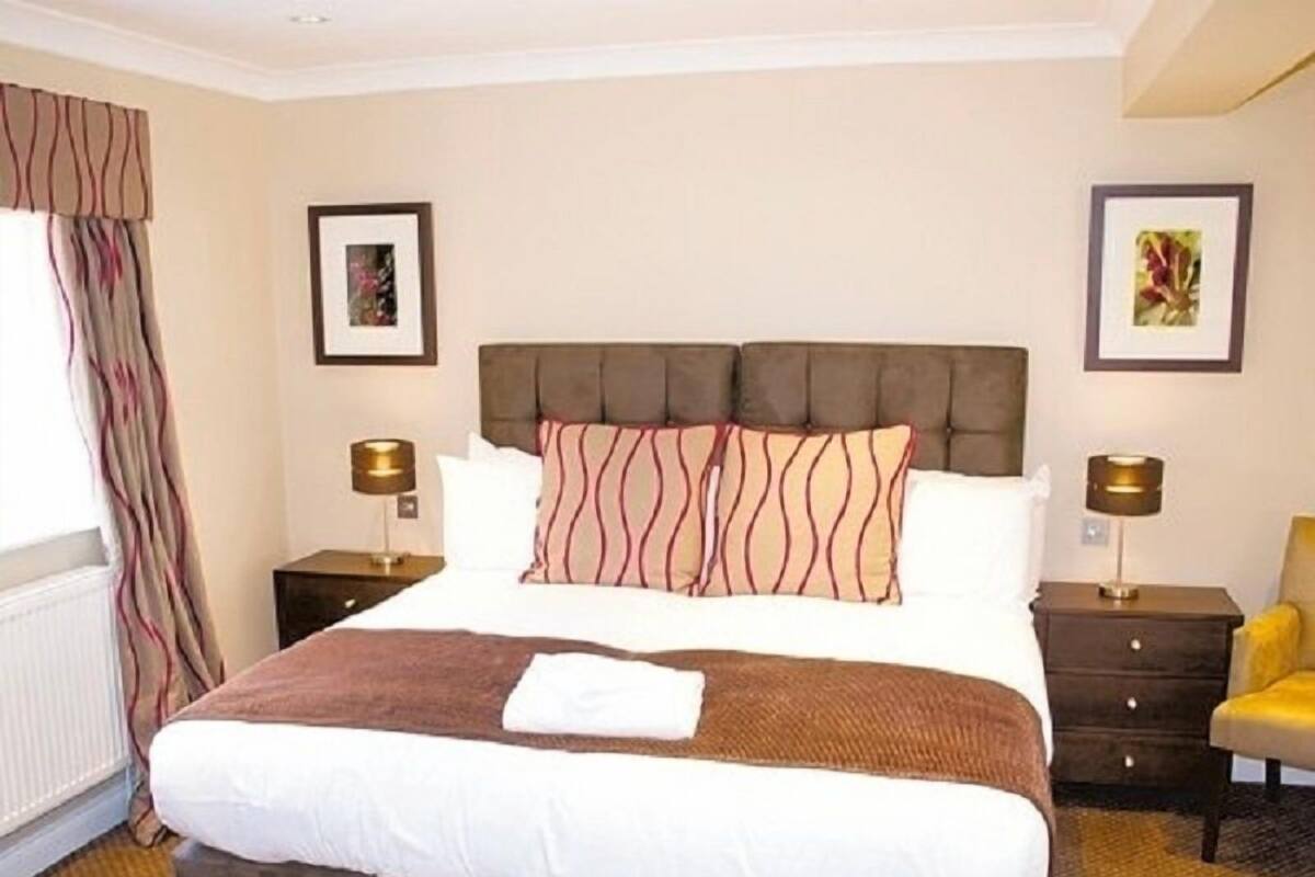 A hotel room with a large bed, two bedside tables, a chair, and two framed pictures on the walls.