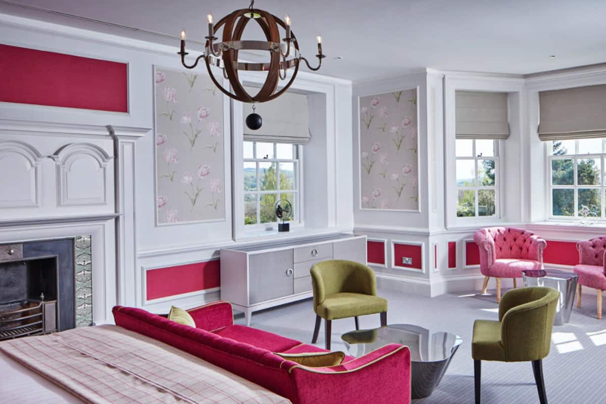 A spacious room with a fireplace, a chandelier, and large windows with floral wallpaper.