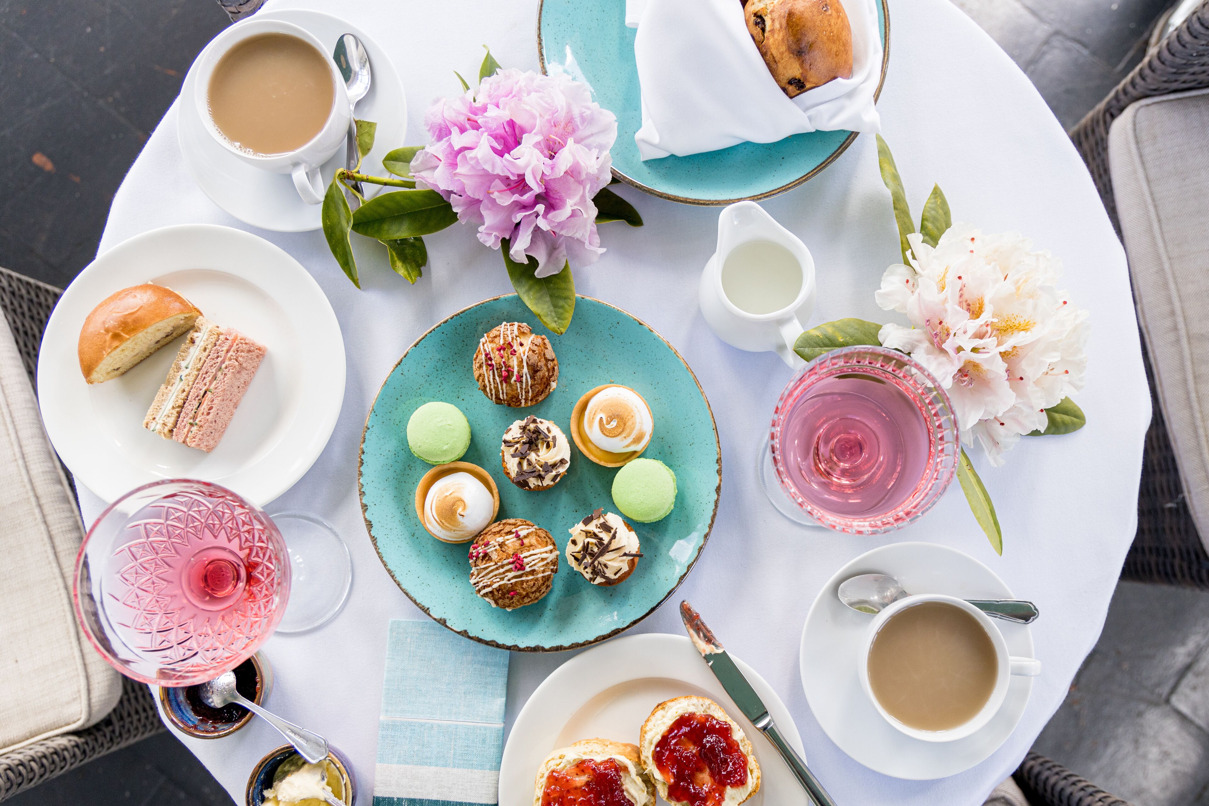 Une table ronde garnie d’une variété de pâtisseries, de boissons et de fleurs.