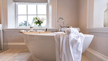 A large freestanding bathtub in a bathroom with a window, a vase of flowers, and a towel on the side.