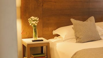 Un lit bien fait, avec une tête de lit en bois, une table de chevet ornée d’un vase de fleurs et des œuvres d’art encadrées accrochées au mur.