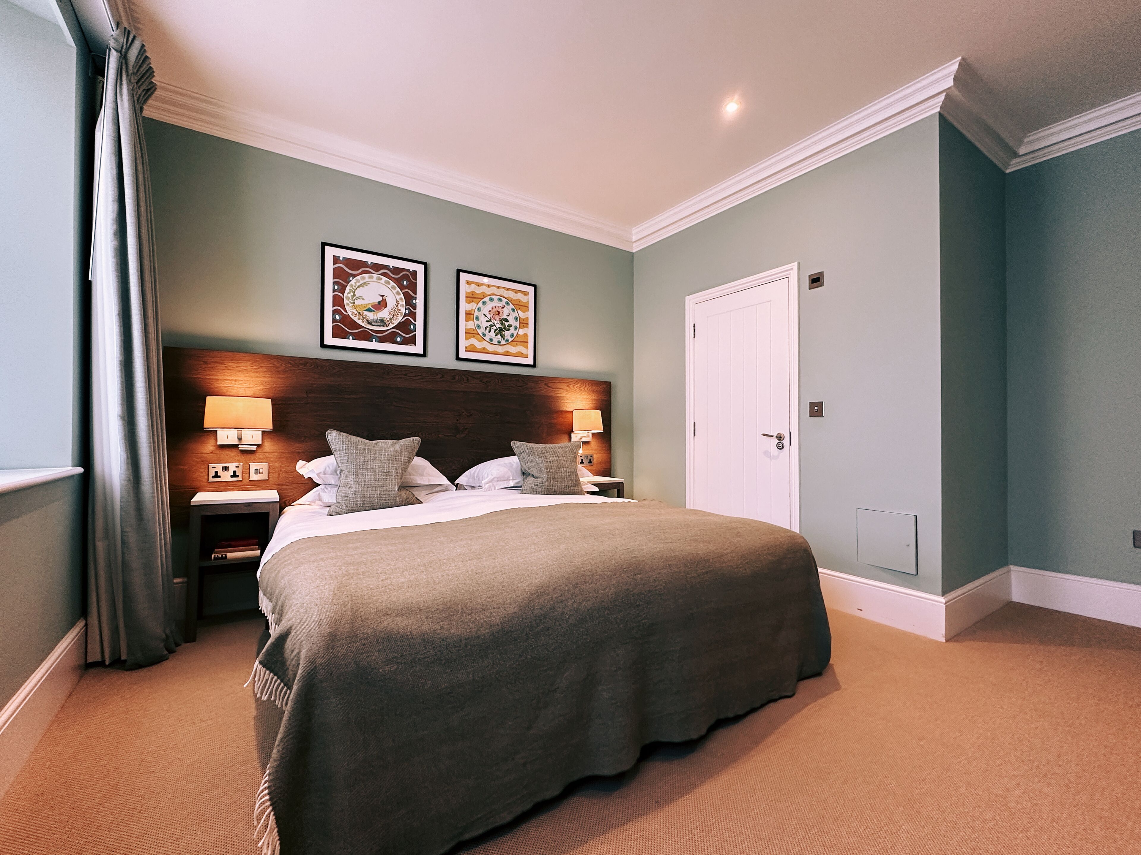 Une chambre à coucher bien rangée, avec un grand lit, deux tables de chevet dotées de lampes et deux tableaux encadrés accrochés au mur.