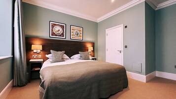 Une chambre à coucher bien rangée, avec un grand lit, deux tables de chevet dotées de lampes et deux tableaux encadrés accrochés au mur.