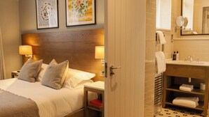 A hotel room with a bed, bedside lamps, a nightstand, a wooden headboard, and a bathroom with a sink, mirror, and towel rack. - The Georgian, Haslemere, Surrey (Haslemere)
