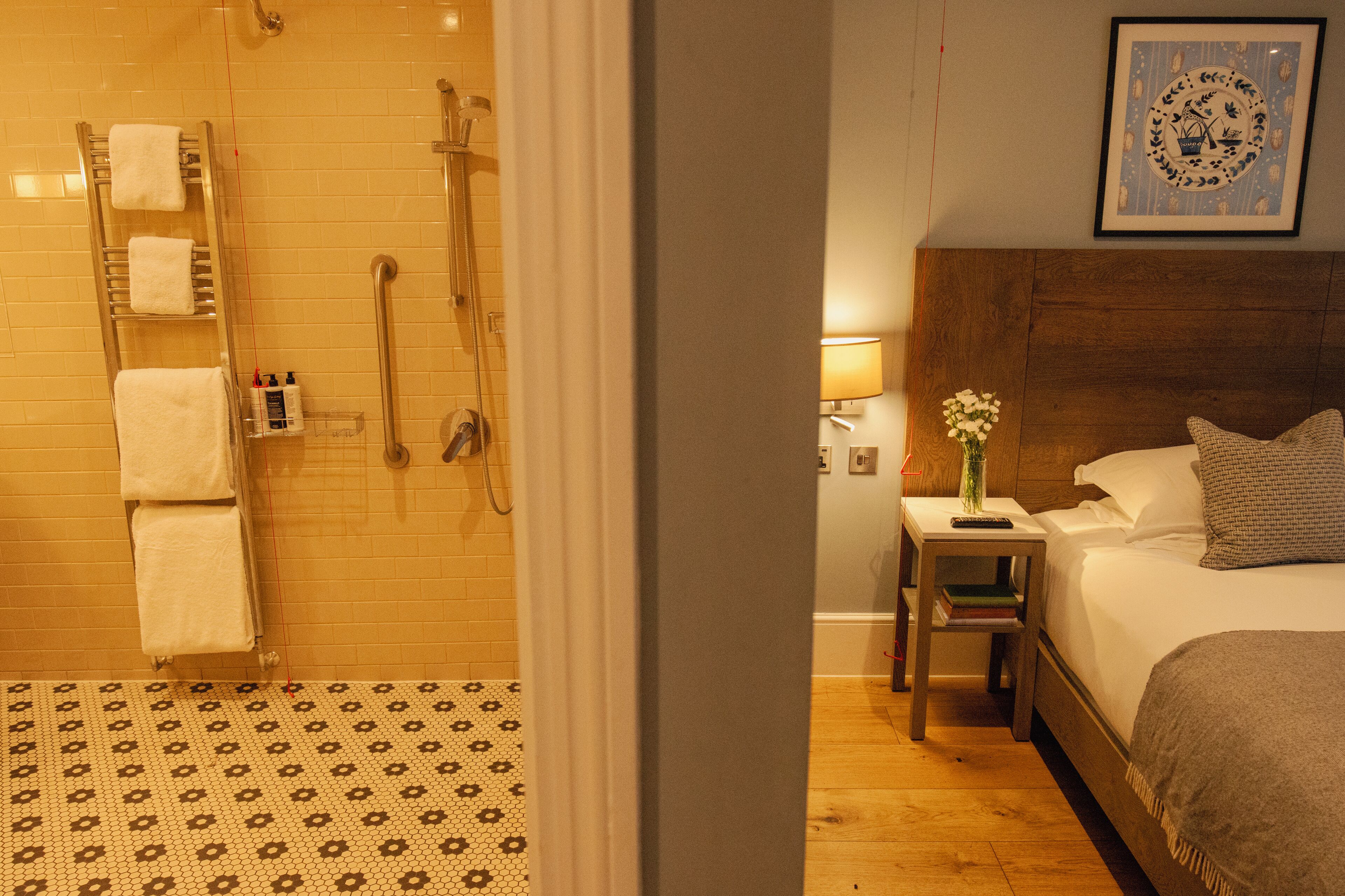 Une chambre d’hôtel avec une douche, une table de chevet avec une lampe, une plante sur la table de chevet et un lit avec des oreillers.