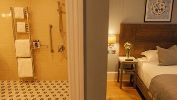 Une chambre d’hôtel avec une douche, une table de chevet avec une lampe, une plante sur la table de chevet et un lit avec des oreillers.